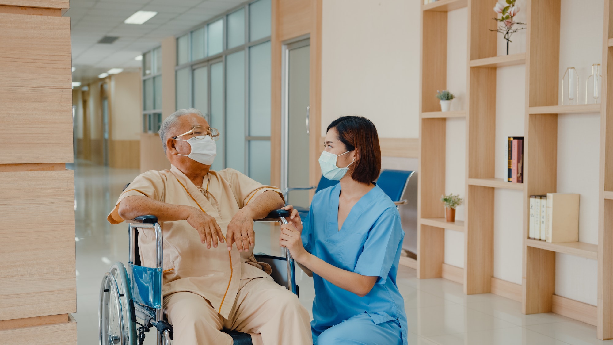 Young Asian woman nurse caregiver wear medical face mask encourage take care her patient explain.